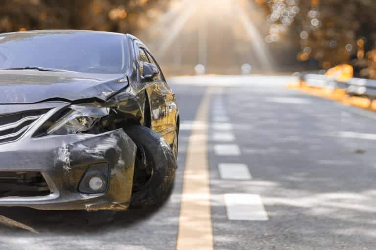Car damaged, alone on rural road, light filtering through trees