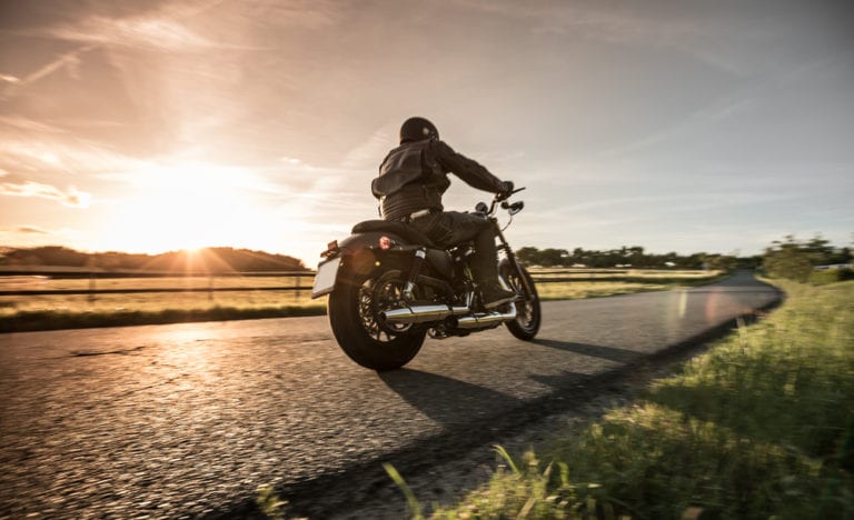 Man riding a motorcycle on rural road at sunset
