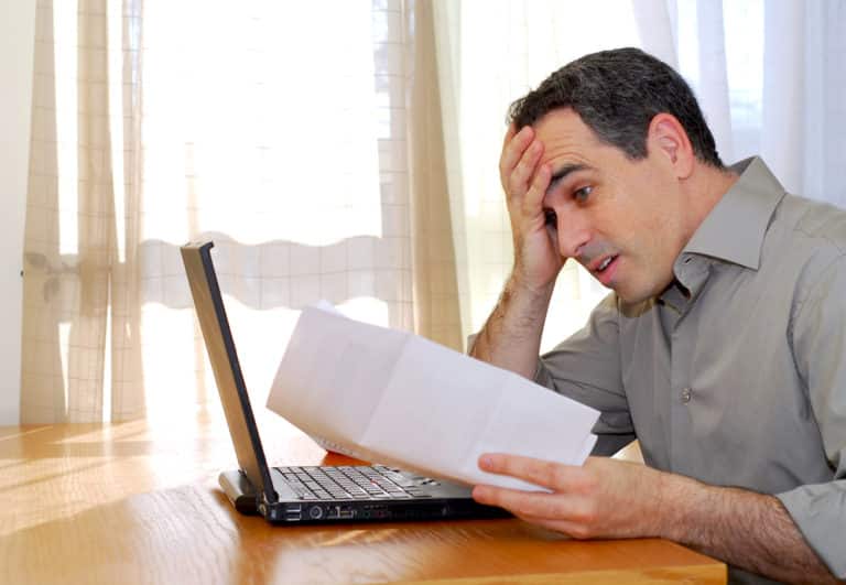 Frustrated man looking at paper, open laptop