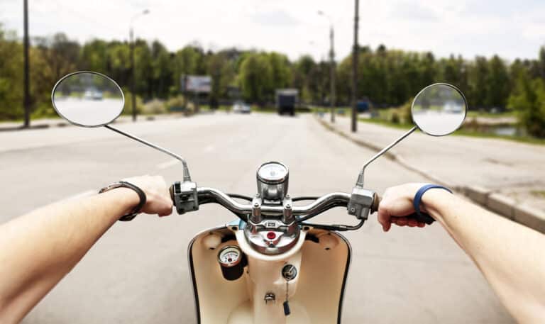 Perspective of moped driver on road holding handlebars