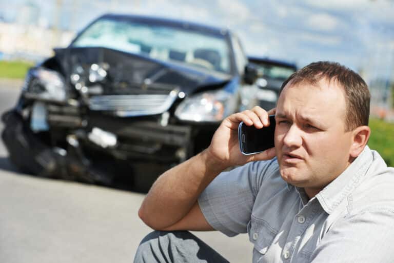 Man talking on phone after car crash, damaged car
