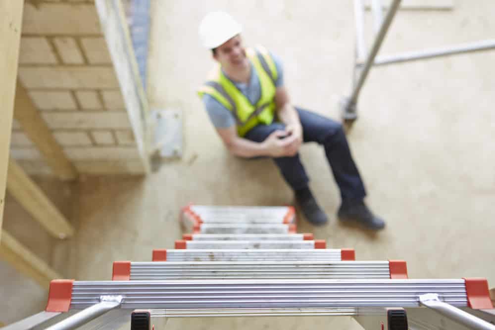 Close-up on ladder, blurry background featuring worker holding injured leg