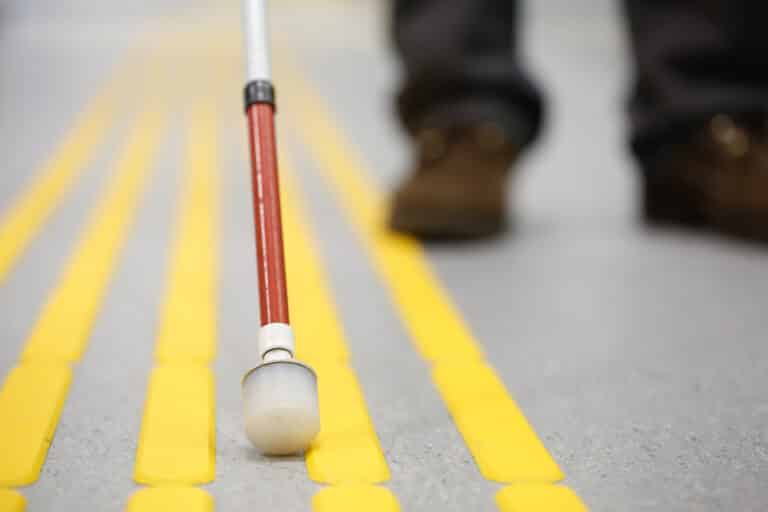 Close-up of blind person walking on pavement using cane