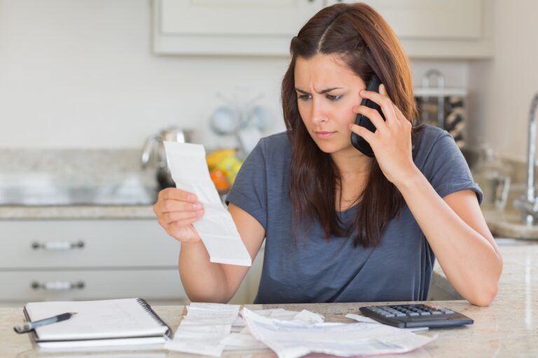 Distressed young woman looking at medical bill while holding phone