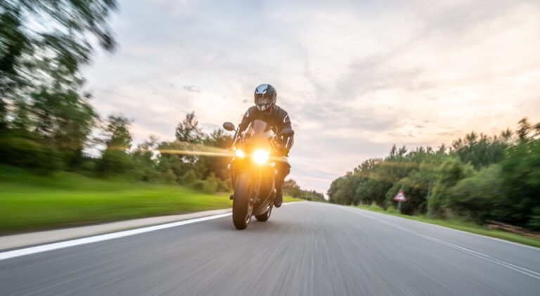 Motorcyclist riding in the evening on empty road, lights on