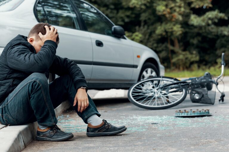 Young man holding head sitting beside car and bike crash aftermath
