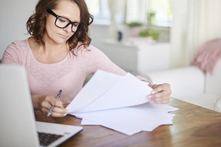 Woman looking at documents on desk, laptop beside